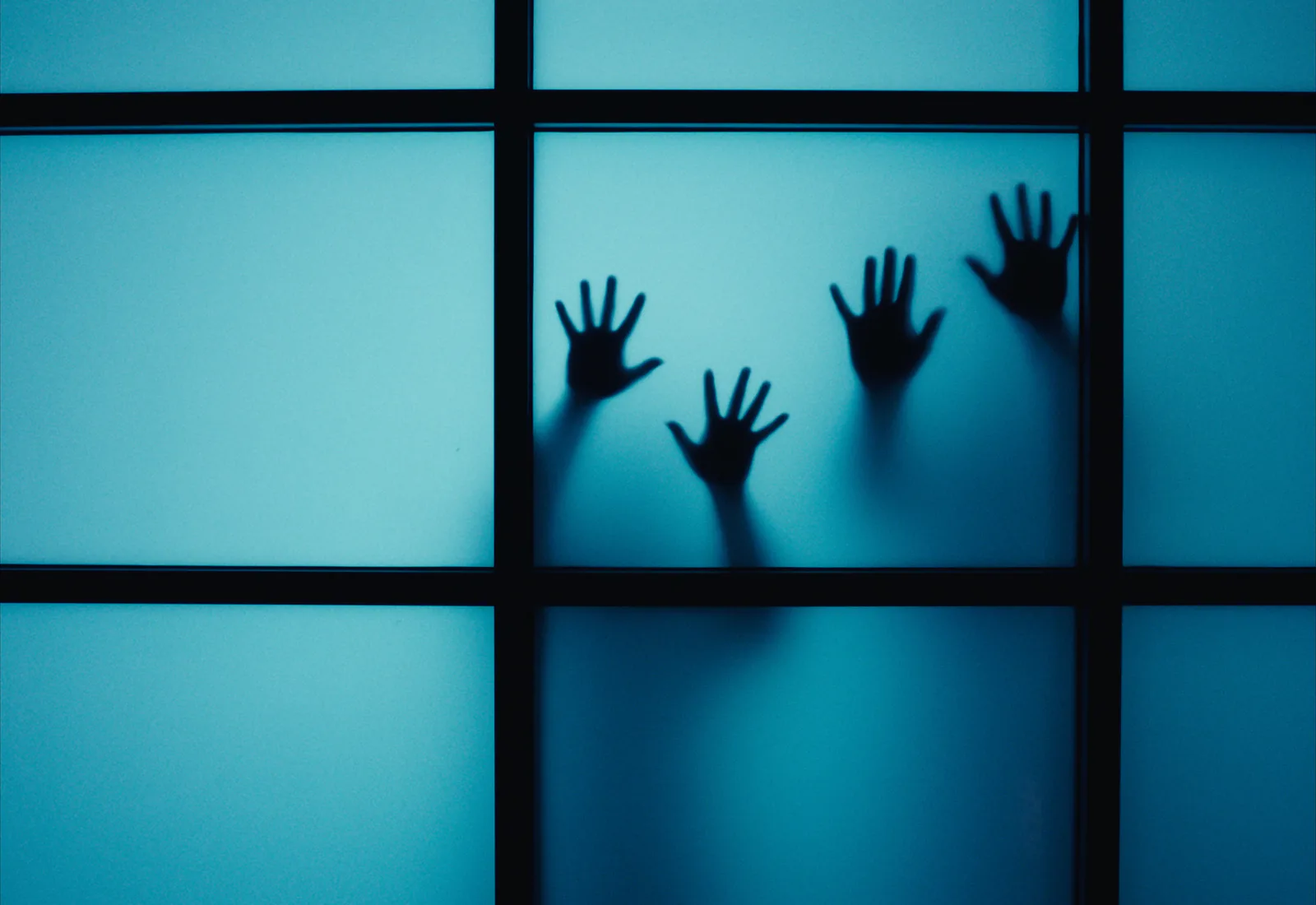 Silhouetted hands pressed against a backlit blue frosted window divided by black glazing bars.